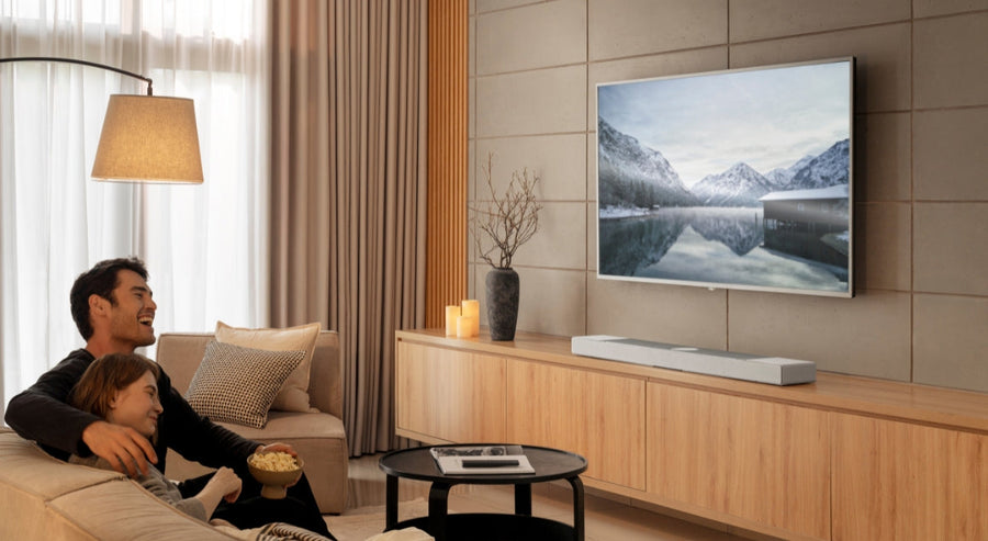 Couple relaxing on a sofa watching TV in a cosy living room with a KEF soundbar on a wooden media unit.