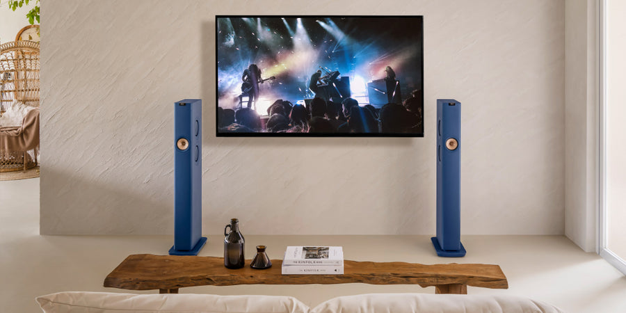 Pair of KEF LS60 Wireless speakers between a TV displaying a live concert in a living room