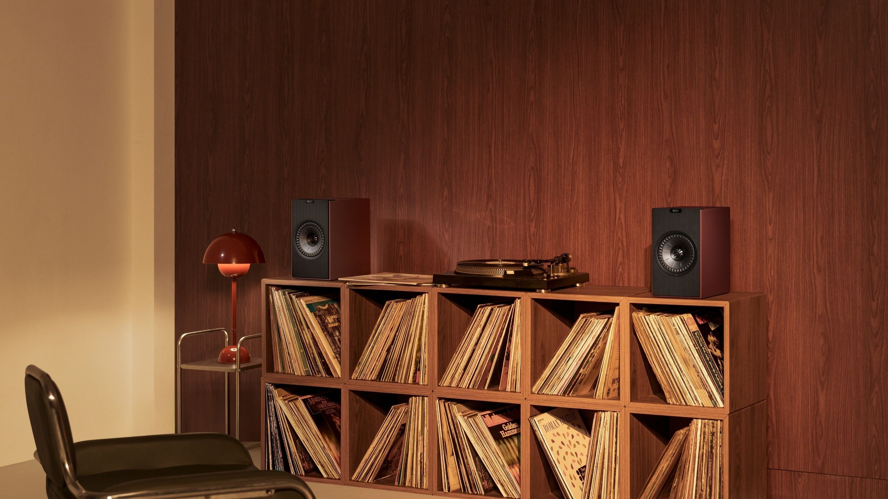 A stylish room showcasing a chair, a bookshelf, and KEF Coda W Bookshelf speakers
