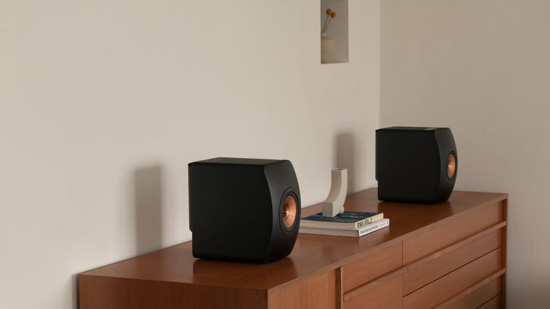 Side angle of KEF LS50 Wireless II speakers placed on a brown sideboard