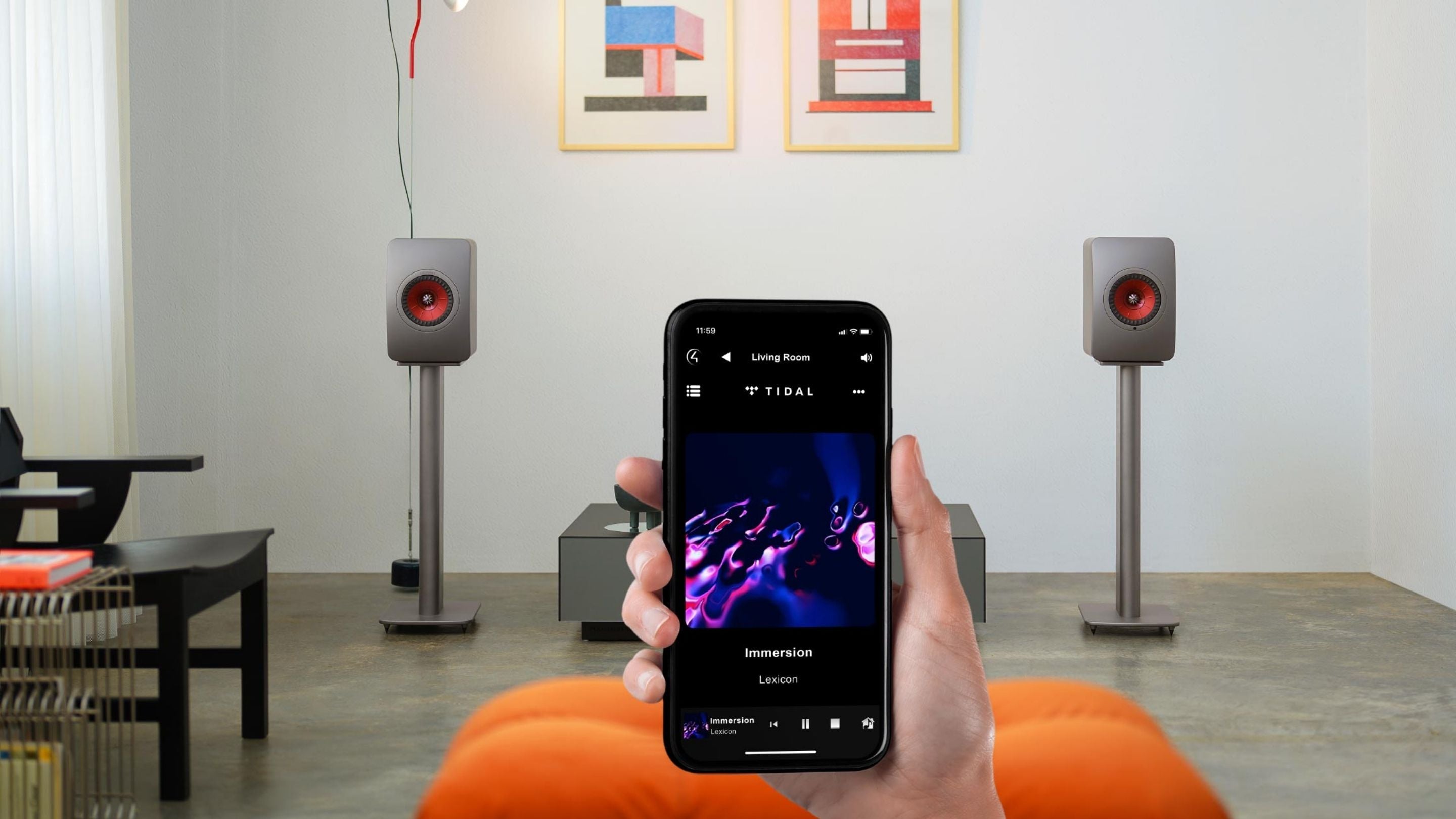 Person holding a smartphone with TIDAL music app on screen in a room with speakers