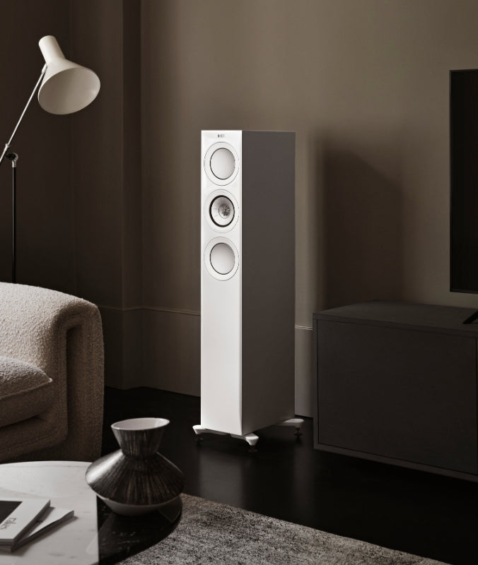 White R series floorstanding speaker next to sofa and TV in living room.