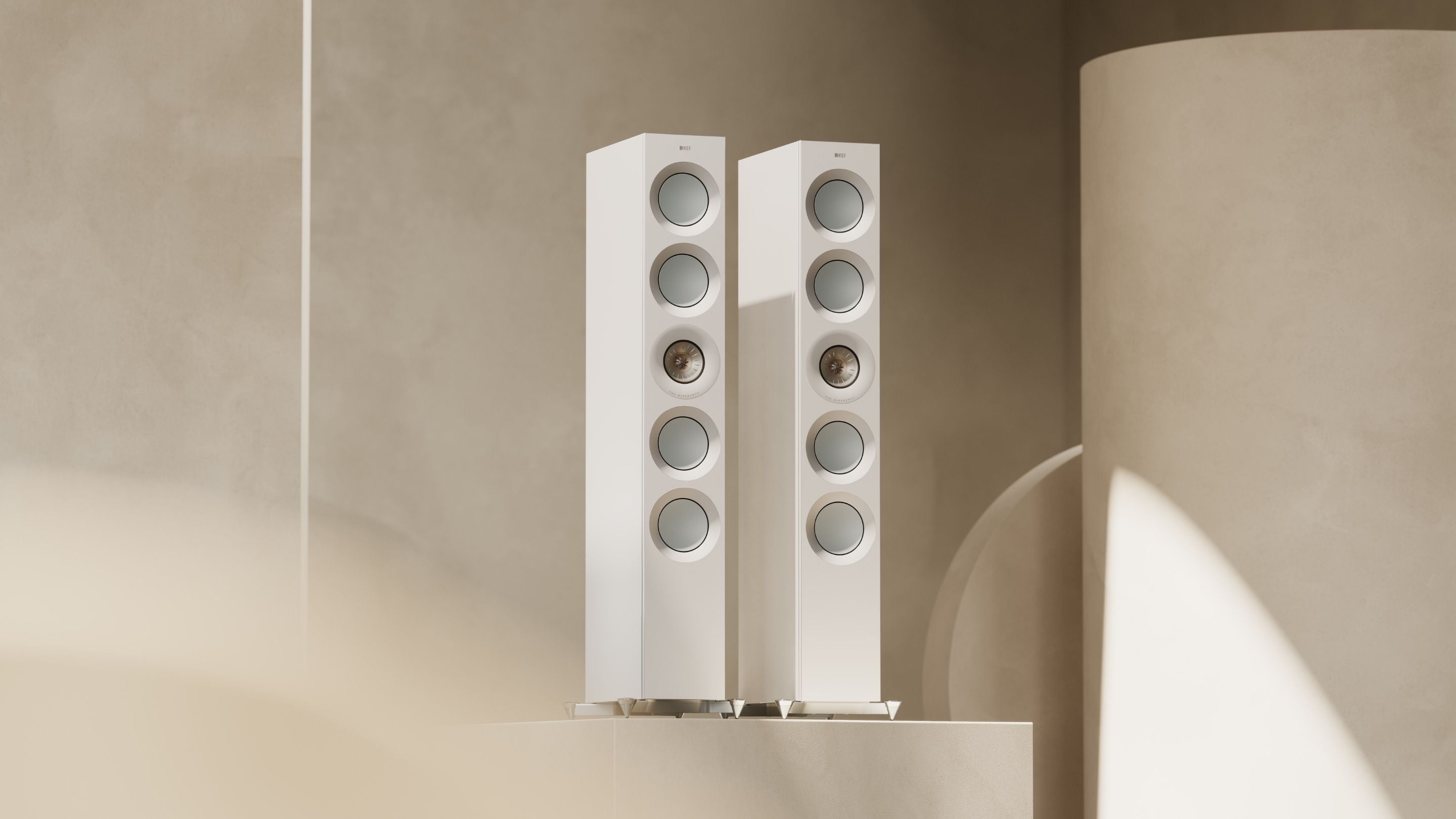 Pair of white The Reference floorstanding speakers with beige background.